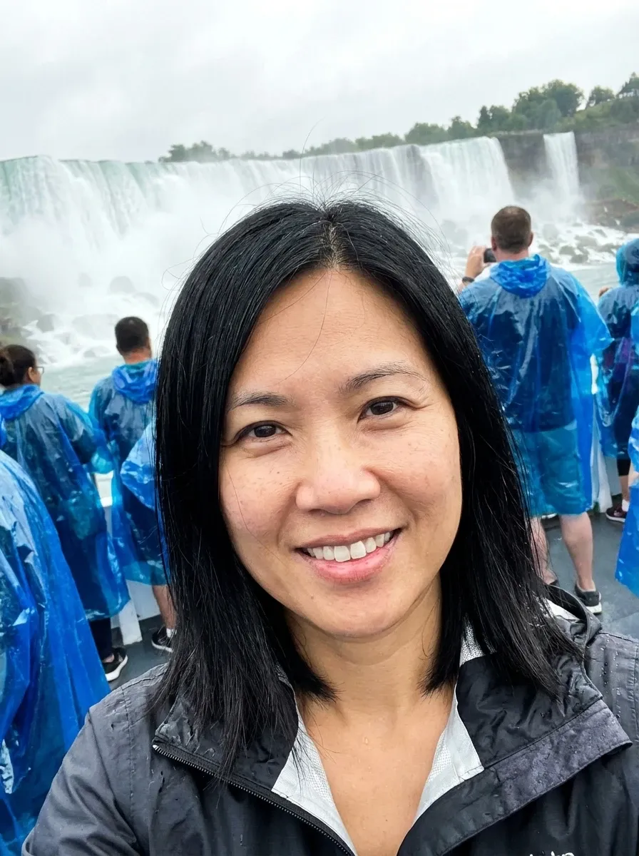 Original selfie input — smiling woman in a gray jacket near a waterfall